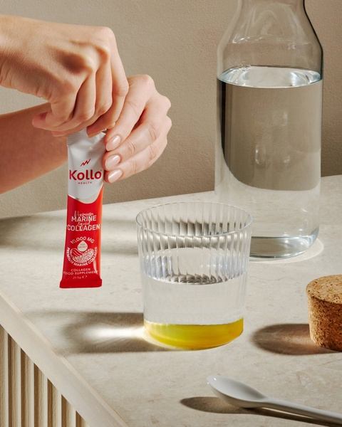 A close-up, high-quality shot showing a person preparing a marine collagen sachet by a glass of water.
